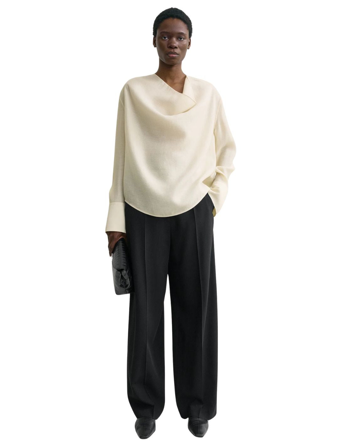 This TOTEME blouse combines refined craftsmanship with effortless style. Crafted from a luxurious blended wool in an elegant ecru shade, its oversized silhouette ensures comfort while maintaining a modern edge. The draped cowl neck creates a sophisticated focal point, complemented by long sleeves finished with buttoned cuffs for a polished look. The curved hem adds subtle fluidity, making this blouse a versatile piece that elevates both casual and formal ensembles with understated elegance.