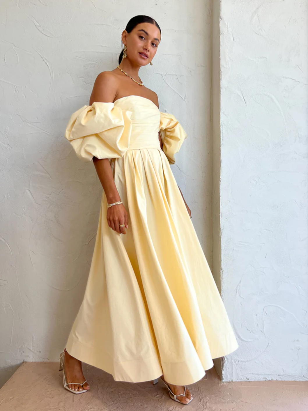 The Matilda Puff Sleeve Midi Dress in Lemon by Leo Lin combines timeless elegance with modern design. Made from soft cotton, it features a strapless straight neckline and delicate puffed short sleeves, complemented by a hand-draped bodice. The dress flows into a gathered, voluminous midi skirt, perfect for garden parties, summer soirees, and wedding celebrations. This dress offers a refined silhouette that enhances confidence and comfort throughout your special occasions.