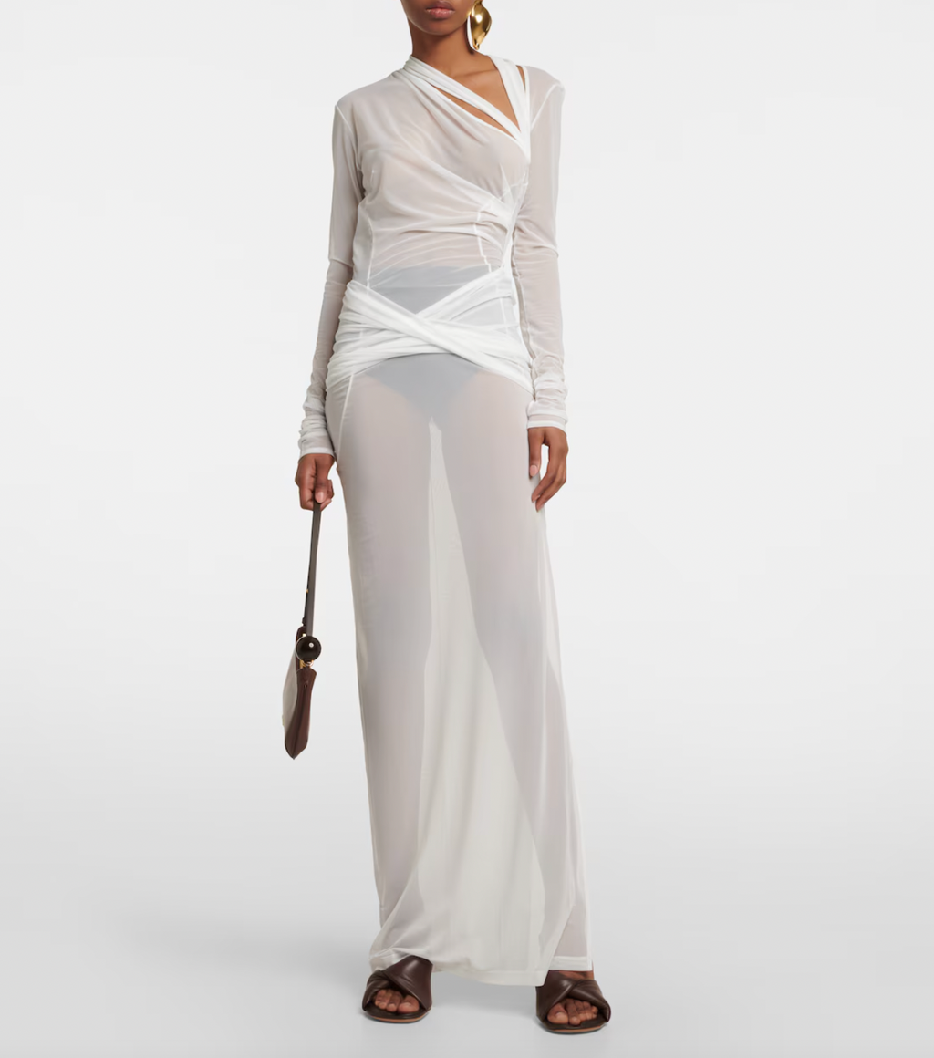 The La Robe Piombone tulle maxi dress by Jacquemus showcases a refined sheer tulle construction with a draped, full-length silhouette that elegantly contours the body. Its asymmetric neckline adds a modern architectural touch, while the long sleeves with thumb holes provide subtle coverage and a distinctive detail. The high-cut side slit enhances movement and introduces a sensual element, making this dress a sophisticated statement for formal occasions or avant-garde styling.
