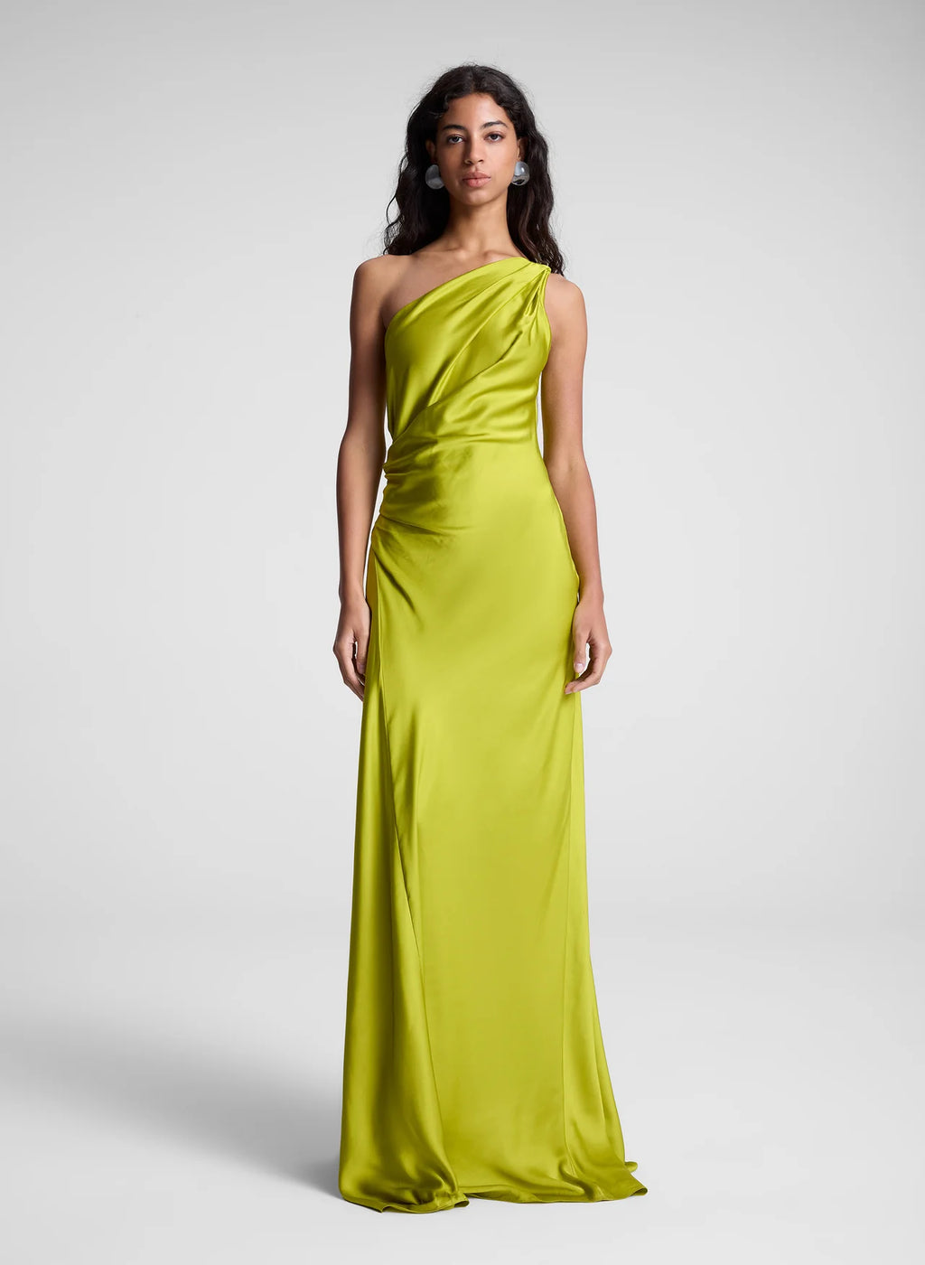 The Aster Satin One Shoulder Gown by A.L.C in radiant chartreuse is expertly crafted from fluid satin, delivering a graceful drape that enhances movement. Its one-shoulder design features delicate pleating at the shoulder and waist, sculpting a refined silhouette with architectural elegance. The asymmetrical cut accentuates the gown’s fluidity, making it a standout piece for sophisticated occasions.