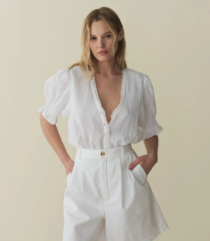 The Karlie Top by Doen is expertly crafted from lightweight ramie, offering a sheer, airy feel. Its Edwardian-inspired silhouette features a plunging V-neckline trimmed with delicate ruffles and intricate pintuck detailing along the yoke, back, and puffed sleeves. A central button line allows versatile styling, whether worn loosely or tucked in, making it an ideal match for high-waisted jeans. This top seamlessly blends timeless romantic details with contemporary functionality.