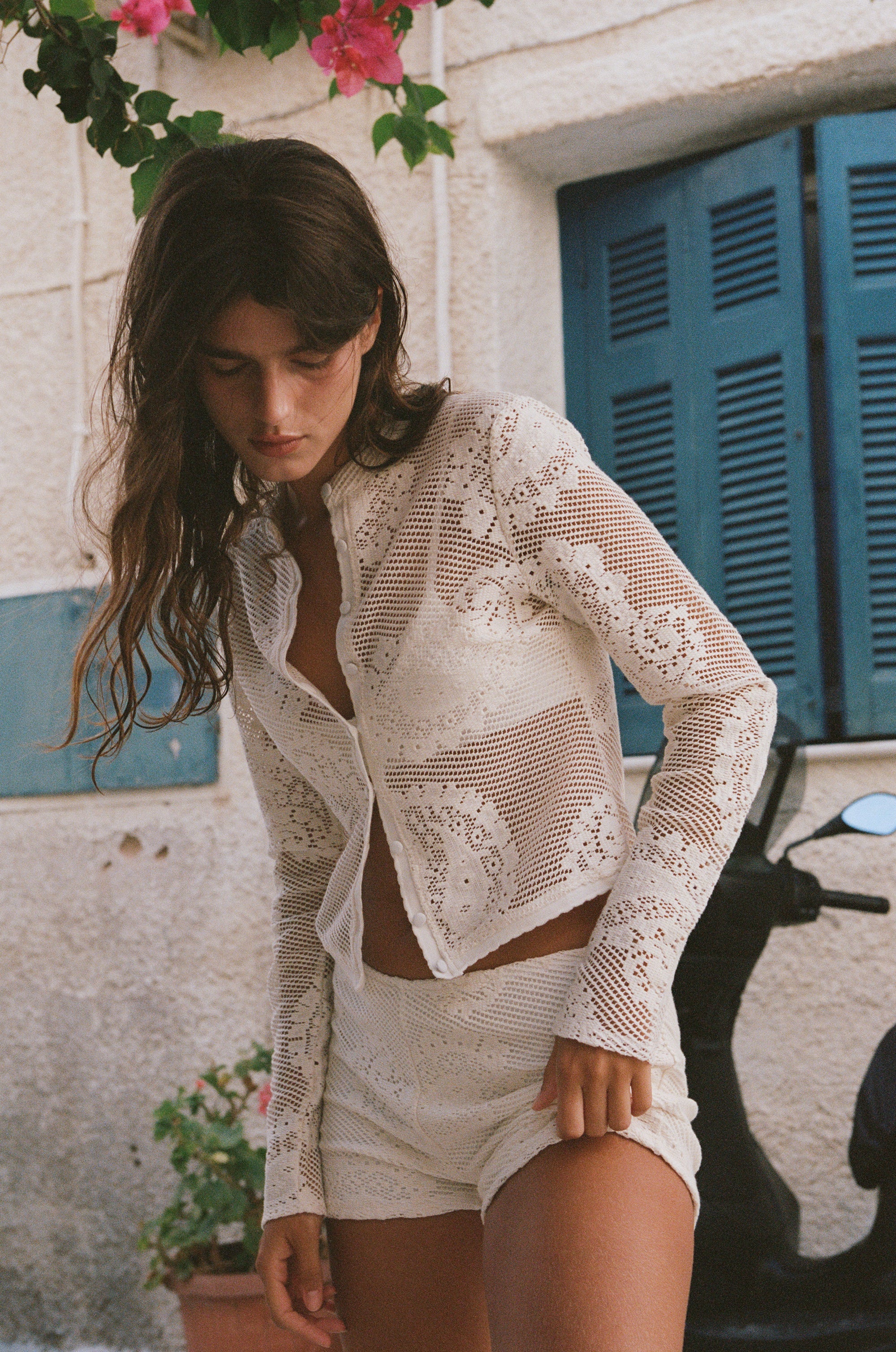 The Dom Top by With Jean is an expertly crafted long-sleeve cardigan with a button-up front and a refined neckline collar. It features delicate scalloped trim and custom hand-drawn crochet lace detailing, combining intricate craftsmanship with timeless style for a sophisticated and elegant look.