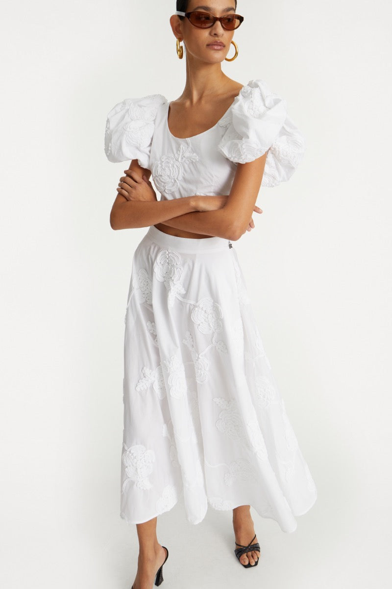 The Flower Maxi Skirt in Bright White combines elegance with comfort through its high-waisted design and voluminous flare, offering a flattering silhouette. Meticulously crafted with tonal floral embroidery, this skirt adds subtle sophistication to any outfit. Soft gathers at the waistband enhance its shape while a concealed side zipper ensures a seamless fit, making it a refined choice for both casual and formal occasions.