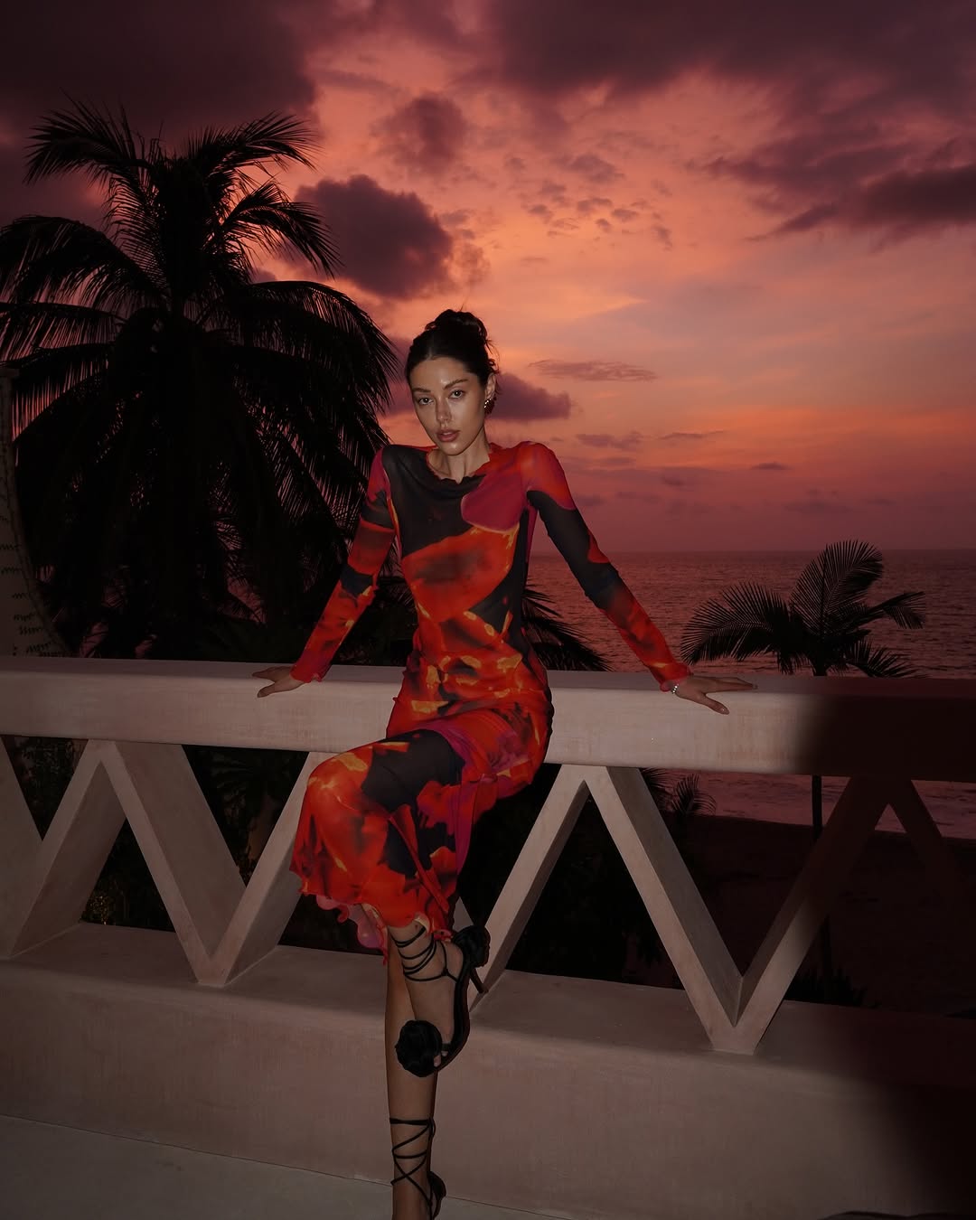 This full-length mesh maxi dress offers a sleek, form-fitting silhouette with its high neckline and long sleeves. Made from sheer, lightweight mesh, it features a unique bold repeat print that varies with each piece. Merrowed ruffle detailing on the sleeves and hem adds elegant sculptural texture. Designed for versatility, this dress effortlessly transitions from daytime sophistication to evening statement wear.