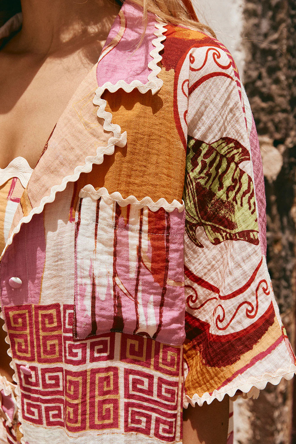 The Kelia Shirt in Theotokos Peach by Sabo is a boxy fit shirt featuring the exclusive Resort&nbsp; print. Made with a blend of viscose and nylon, this shirt offers a comfortable fit and stylish details such as a collar, low lapel, and ric rac trim. Perfect for adding a touch of unique elegance to your wardrobe.