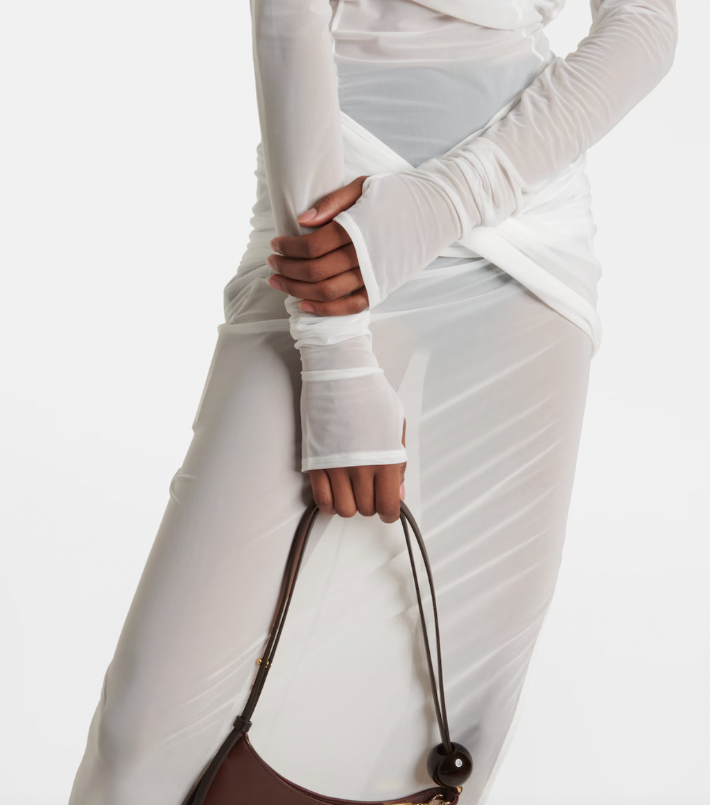 The La Robe Piombone tulle maxi dress by Jacquemus showcases a refined sheer tulle construction with a draped, full-length silhouette that elegantly contours the body. Its asymmetric neckline adds a modern architectural touch, while the long sleeves with thumb holes provide subtle coverage and a distinctive detail. The high-cut side slit enhances movement and introduces a sensual element, making this dress a sophisticated statement for formal occasions or avant-garde styling.