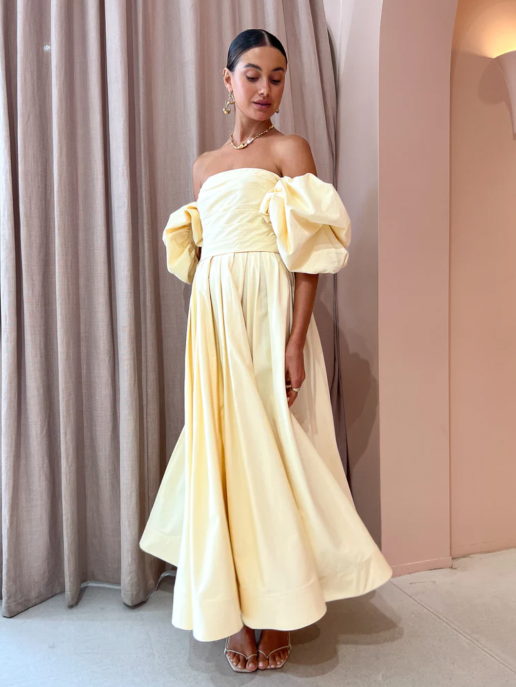 The Matilda Puff Sleeve Midi Dress in Lemon by Leo Lin combines timeless elegance with modern design. Made from soft cotton, it features a strapless straight neckline and delicate puffed short sleeves, complemented by a hand-draped bodice. The dress flows into a gathered, voluminous midi skirt, perfect for garden parties, summer soirees, and wedding celebrations. This dress offers a refined silhouette that enhances confidence and comfort throughout your special occasions.