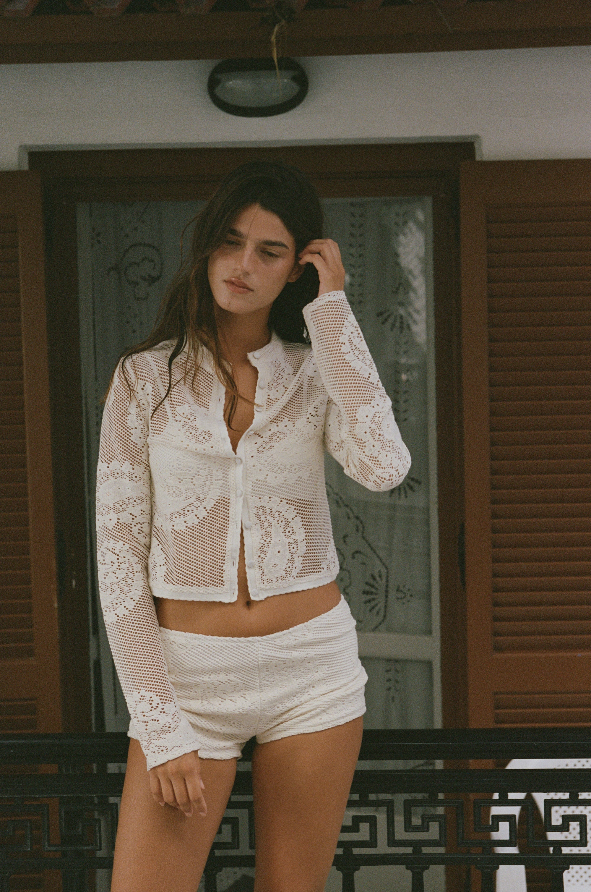 The Dom Top by With Jean is an expertly crafted long-sleeve cardigan with a button-up front and a refined neckline collar. It features delicate scalloped trim and custom hand-drawn crochet lace detailing, combining intricate craftsmanship with timeless style for a sophisticated and elegant look.