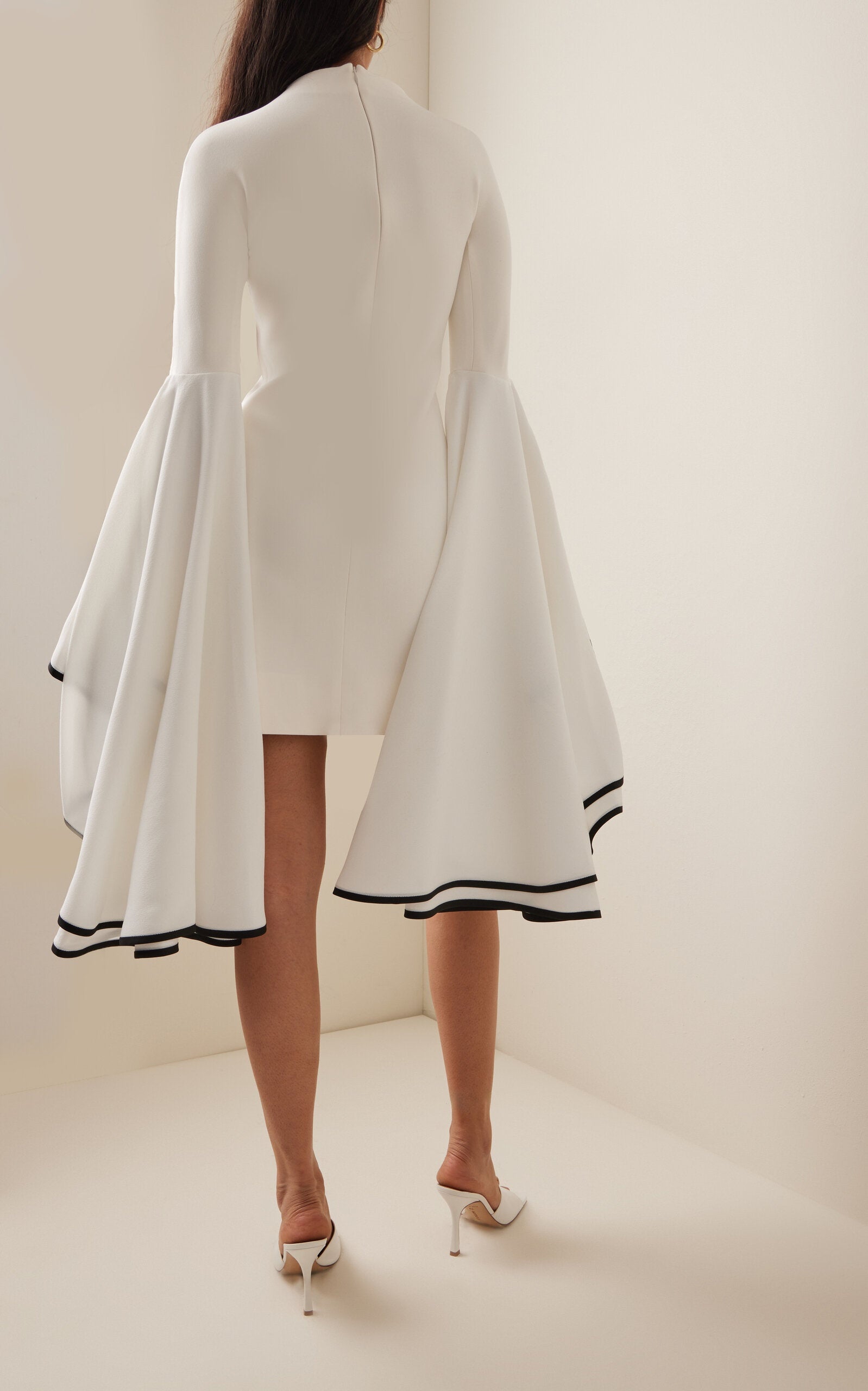 This Stretch Crepe Sleeve Dress by Proenza Schouler features a slim fit with a mock neck and exaggerated bell sleeves accented by contrast cuff trim. The mini hem and concealed back zip create a streamlined silhouette, designed to fit true to size. Pair it with statement heels in a matching colorway and style your hair in a sleek low bun for an elegant, polished look. Unlined for lightweight comfort, it’s perfect for occasions that call for refined sophistication.