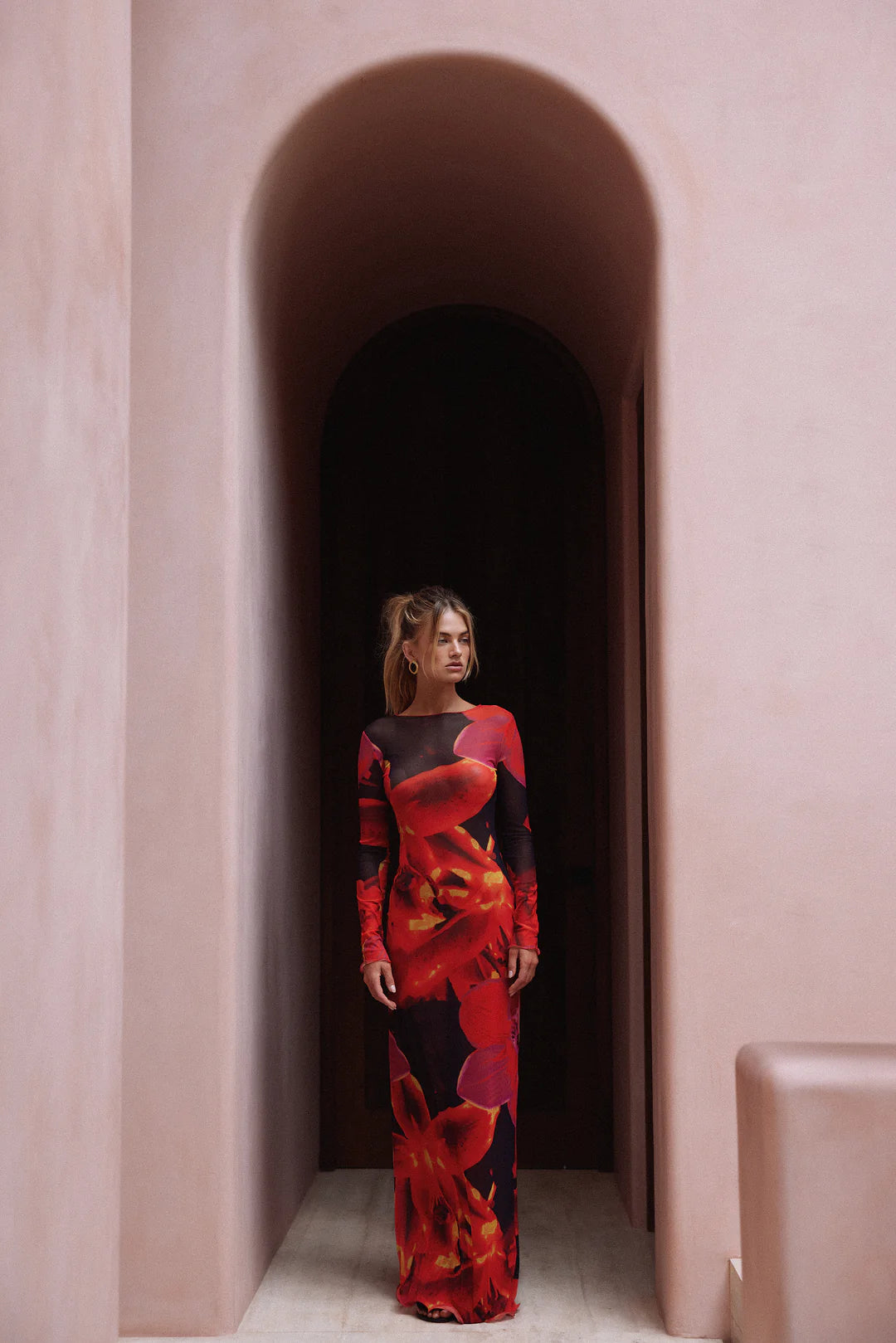 This full-length mesh maxi dress offers a sleek, form-fitting silhouette with its high neckline and long sleeves. Made from sheer, lightweight mesh, it features a unique bold repeat print that varies with each piece. Merrowed ruffle detailing on the sleeves and hem adds elegant sculptural texture. Designed for versatility, this dress effortlessly transitions from daytime sophistication to evening statement wear.