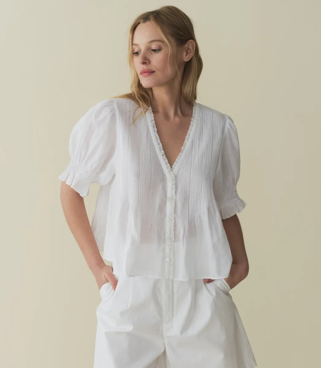 The Karlie Top by Doen is expertly crafted from lightweight ramie, offering a sheer, airy feel. Its Edwardian-inspired silhouette features a plunging V-neckline trimmed with delicate ruffles and intricate pintuck detailing along the yoke, back, and puffed sleeves. A central button line allows versatile styling, whether worn loosely or tucked in, making it an ideal match for high-waisted jeans. This top seamlessly blends timeless romantic details with contemporary functionality.