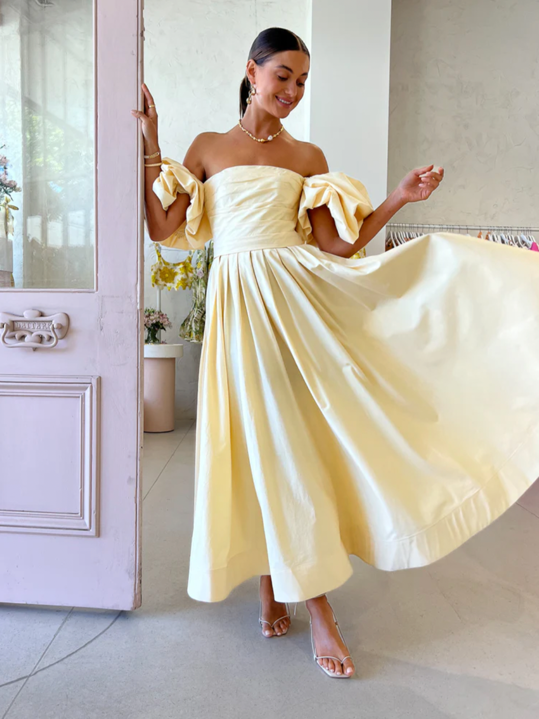 The Matilda Puff Sleeve Midi Dress in Lemon by Leo Lin combines timeless elegance with modern design. Made from soft cotton, it features a strapless straight neckline and delicate puffed short sleeves, complemented by a hand-draped bodice. The dress flows into a gathered, voluminous midi skirt, perfect for garden parties, summer soirees, and wedding celebrations. This dress offers a refined silhouette that enhances confidence and comfort throughout your special occasions.