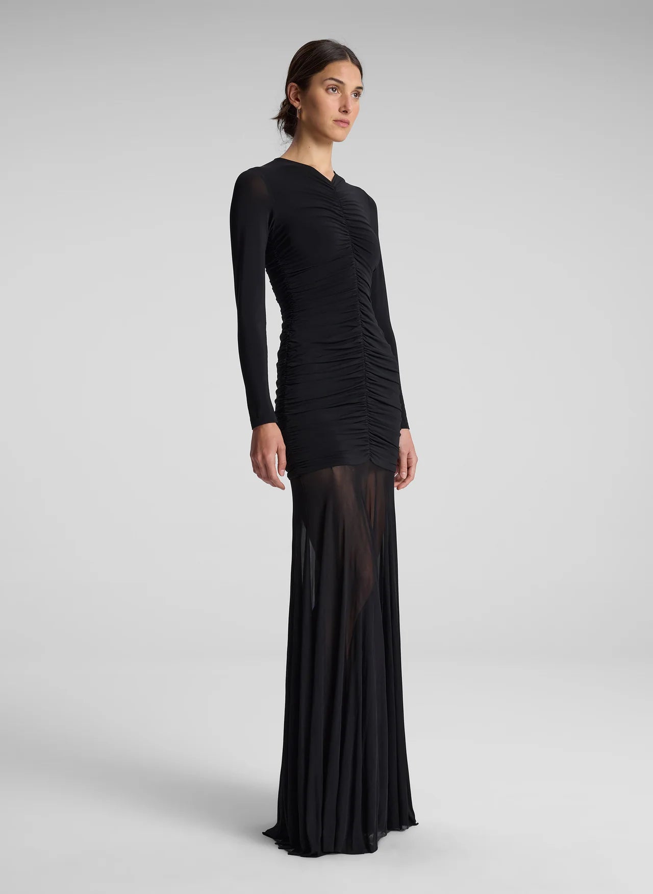 The Fawn Ruched Mesh Maxi Dress combines elegance and contemporary design through its sheer jersey fabric in timeless black. This full-length gown showcases a v-neckline with a delicately ruched bodice that enhances the silhouette, complemented by sheer sleeves for subtle sophistication. The pleated sheer skirt moves gracefully, offering fluidity and refined style suitable for formal occasions or evening wear.