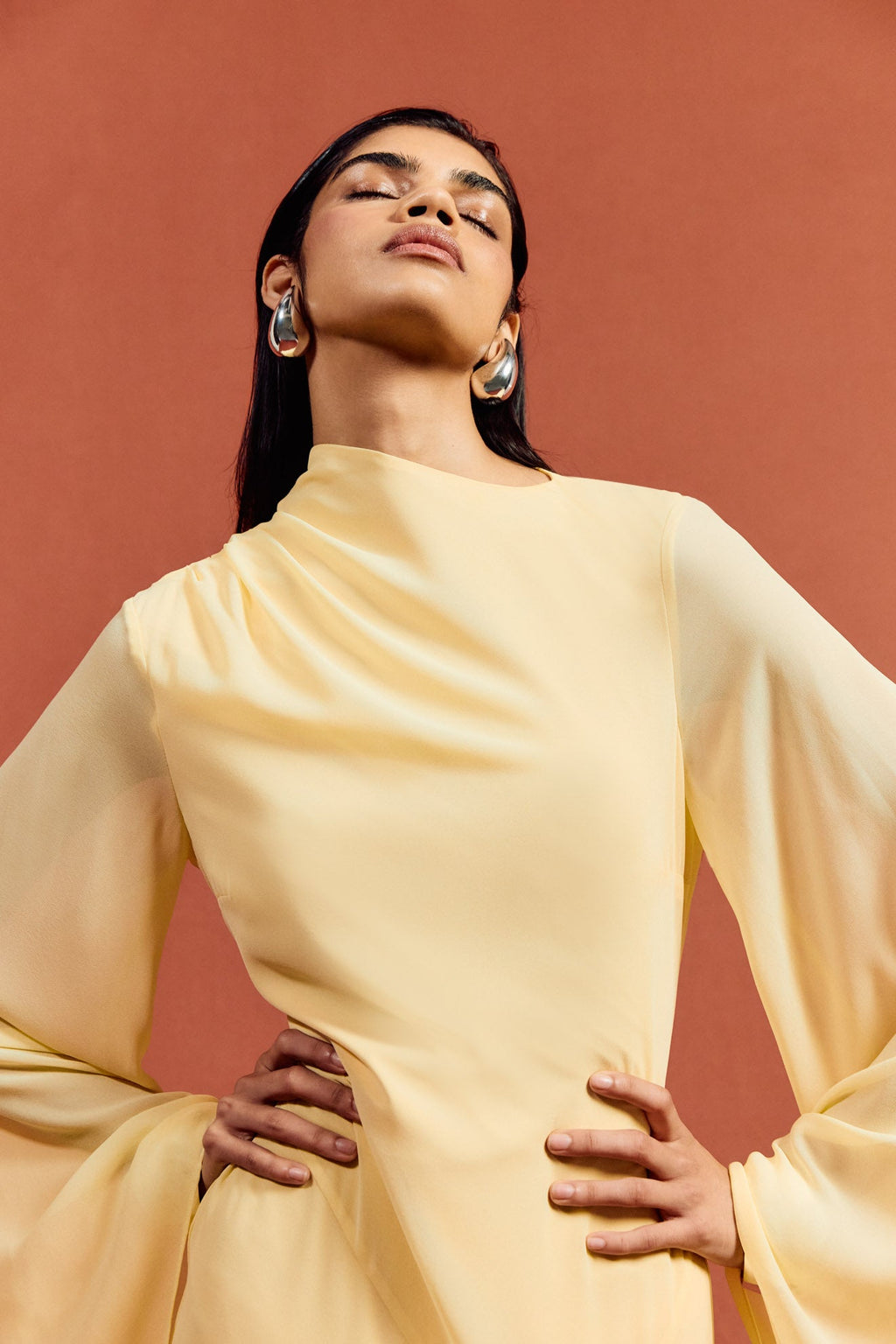 The Hausos Maxi Dress in Sherbet Yellow features an elegant chiffon construction with a floor-length silhouette, creating a graceful presence. Its distinctive dipped waist seam and draped skirt with godet panels add dynamic movement and refined shape. The asymmetric neckline delivers a modern edge, while the long pagoda sleeves introduce dramatic flare for a sophisticated, fashion-forward statement. Ideal for formal occasions, this dress combines fluidity and structure with expert design details.