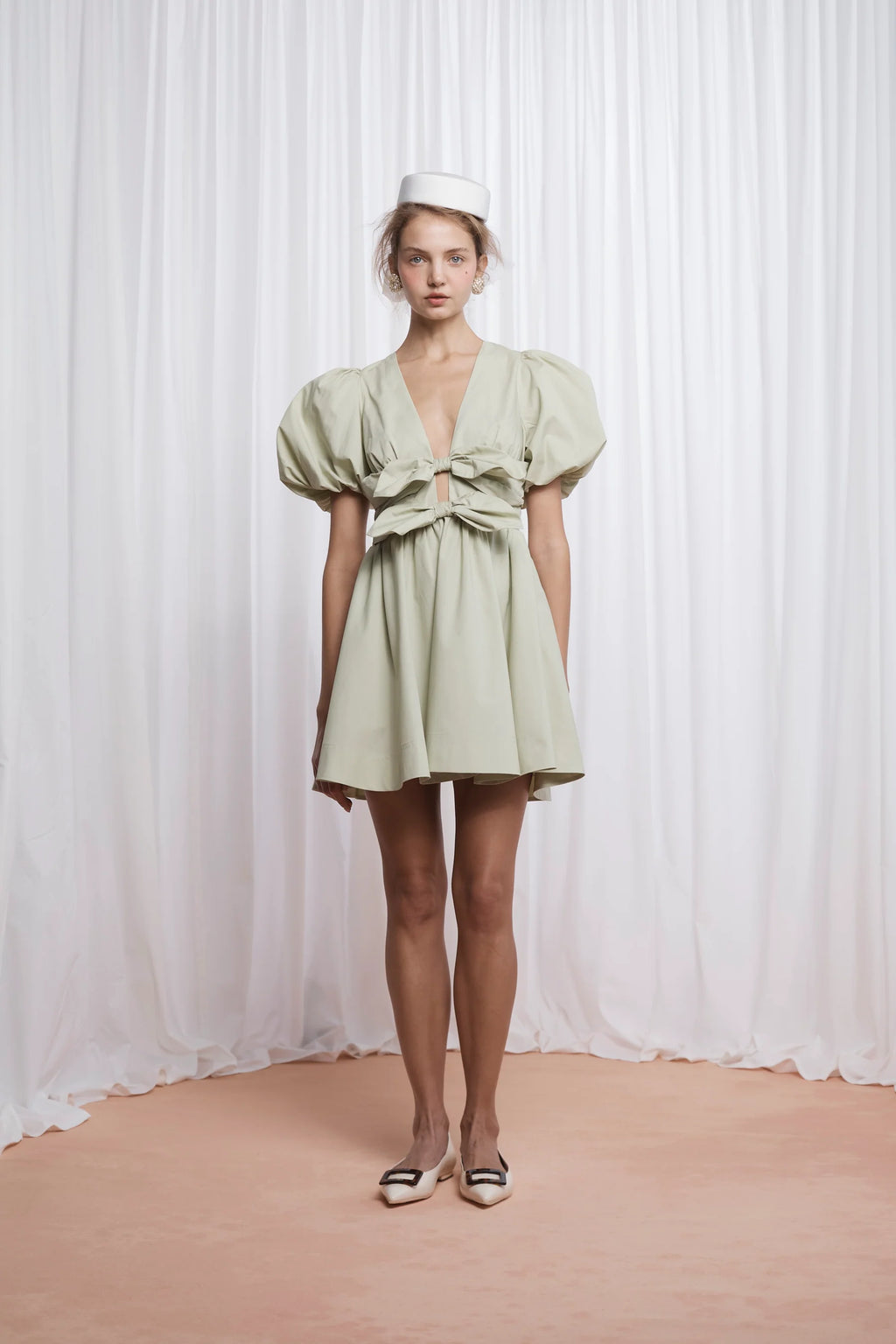The Devon Mini Dress in pistachio combines expert tailoring with comfort, crafted from butter-soft cotton poplin. Its deep V-neckline and blousy puff sleeves create a flattering silhouette, while the double bow front adds a refined, feminine touch. Designed for ease, it features an elasticated back, discreet side seam zip, and practical pockets. Fully lined for smooth wear, this dress delivers both style and function in a lightweight, breathable fabric.