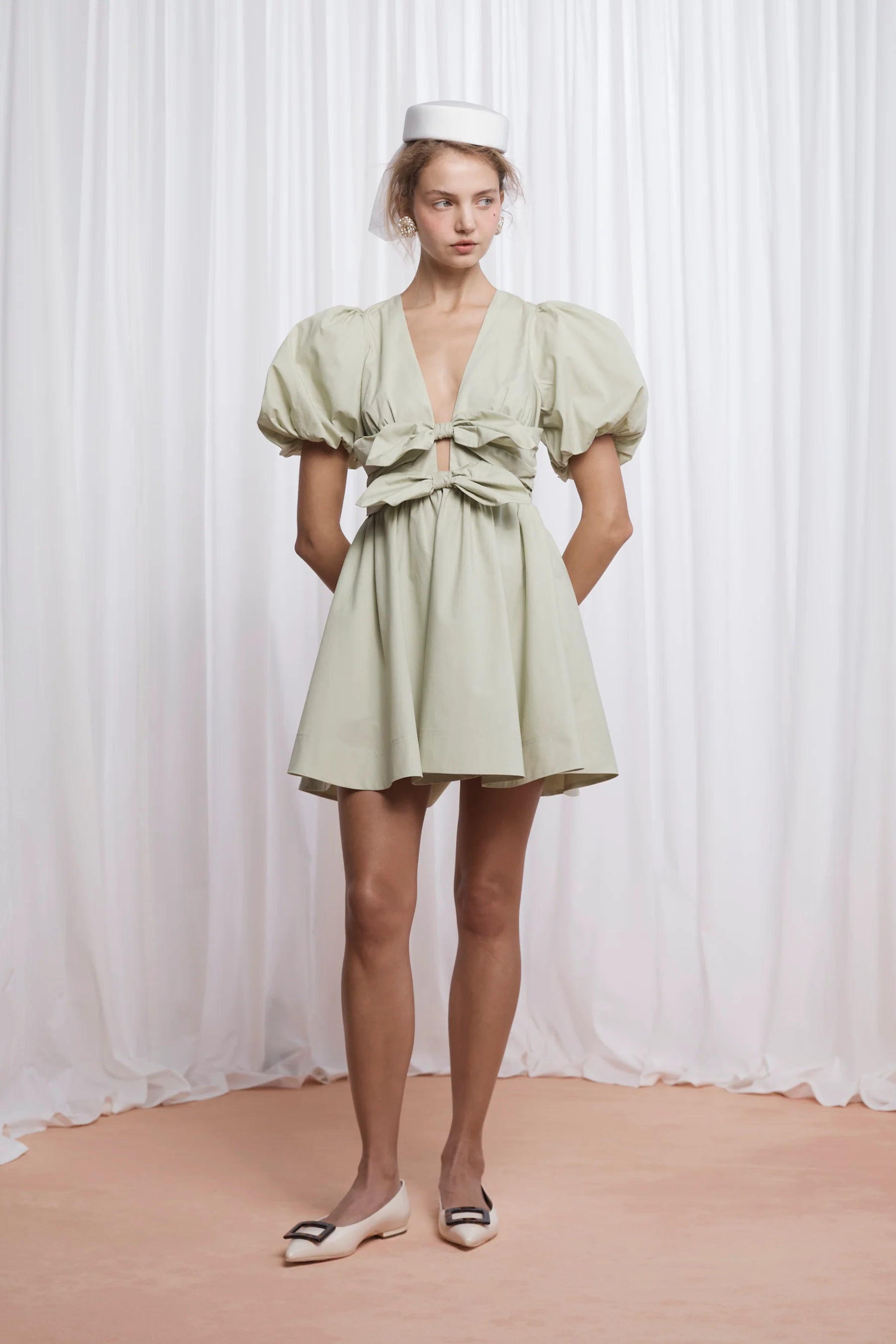 The Devon Mini Dress in pistachio combines expert tailoring with comfort, crafted from butter-soft cotton poplin. Its deep V-neckline and blousy puff sleeves create a flattering silhouette, while the double bow front adds a refined, feminine touch. Designed for ease, it features an elasticated back, discreet side seam zip, and practical pockets. Fully lined for smooth wear, this dress delivers both style and function in a lightweight, breathable fabric.