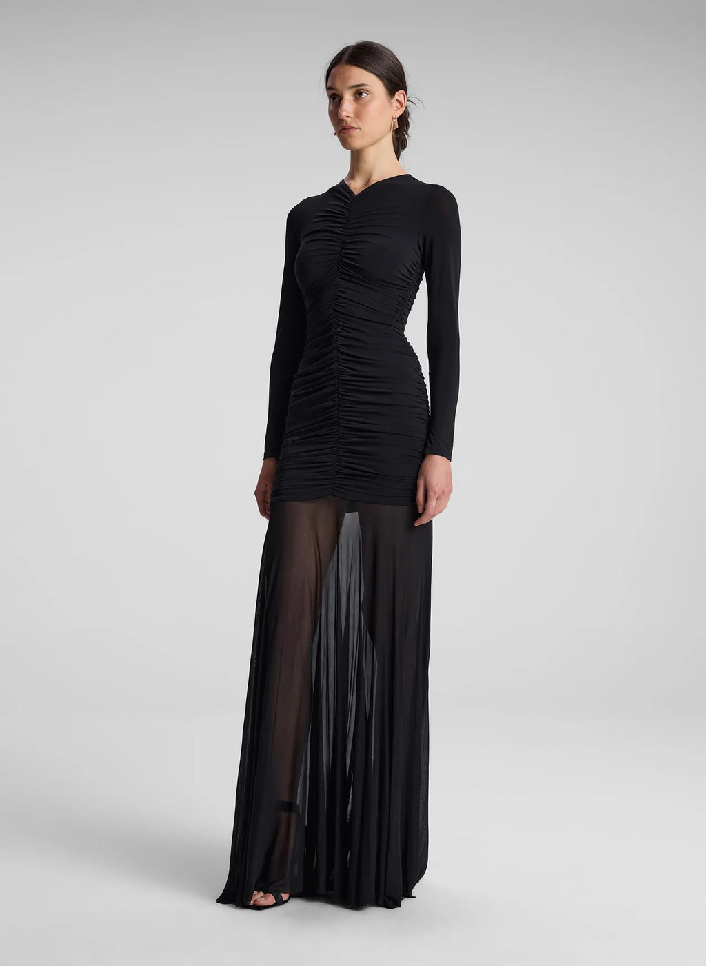 The Fawn Ruched Mesh Maxi Dress combines elegance and contemporary design through its sheer jersey fabric in timeless black. This full-length gown showcases a v-neckline with a delicately ruched bodice that enhances the silhouette, complemented by sheer sleeves for subtle sophistication. The pleated sheer skirt moves gracefully, offering fluidity and refined style suitable for formal occasions or evening wear.