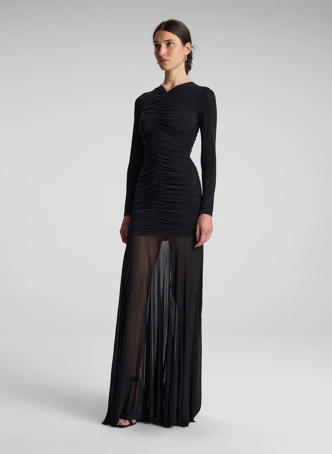 The Fawn Ruched Mesh Maxi Dress combines elegance and contemporary design through its sheer jersey fabric in timeless black. This full-length gown showcases a v-neckline with a delicately ruched bodice that enhances the silhouette, complemented by sheer sleeves for subtle sophistication. The pleated sheer skirt moves gracefully, offering fluidity and refined style suitable for formal occasions or evening wear.
