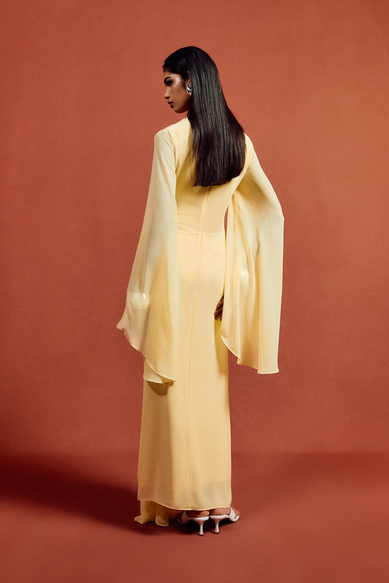 The Hausos Maxi Dress in Sherbet Yellow features an elegant chiffon construction with a floor-length silhouette, creating a graceful presence. Its distinctive dipped waist seam and draped skirt with godet panels add dynamic movement and refined shape. The asymmetric neckline delivers a modern edge, while the long pagoda sleeves introduce dramatic flare for a sophisticated, fashion-forward statement. Ideal for formal occasions, this dress combines fluidity and structure with expert design details.