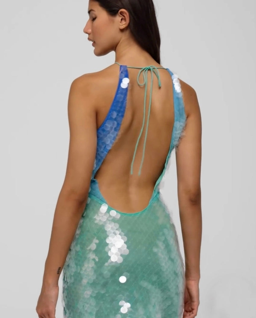 The Kiki Dress captivates with its molten sequin ombré, flowing seamlessly from blue to green for a striking summer soirée look. Expertly bias-cut, it contours the body with a flattering drape that highlights the luxe fabric’s fluidity. Featuring a sensual plunging back and dramatic cowl neckline, this dress embodies refined elegance and vibrant energy, perfect for making a lasting impression on warm, lively nights.