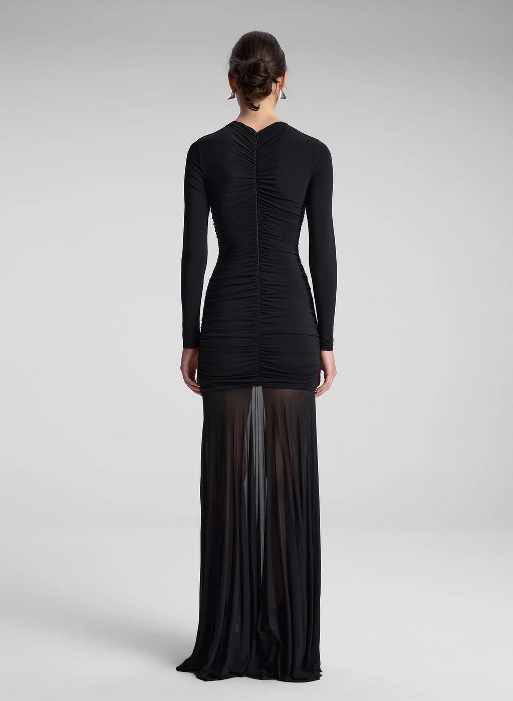The Fawn Ruched Mesh Maxi Dress combines elegance and contemporary design through its sheer jersey fabric in timeless black. This full-length gown showcases a v-neckline with a delicately ruched bodice that enhances the silhouette, complemented by sheer sleeves for subtle sophistication. The pleated sheer skirt moves gracefully, offering fluidity and refined style suitable for formal occasions or evening wear.