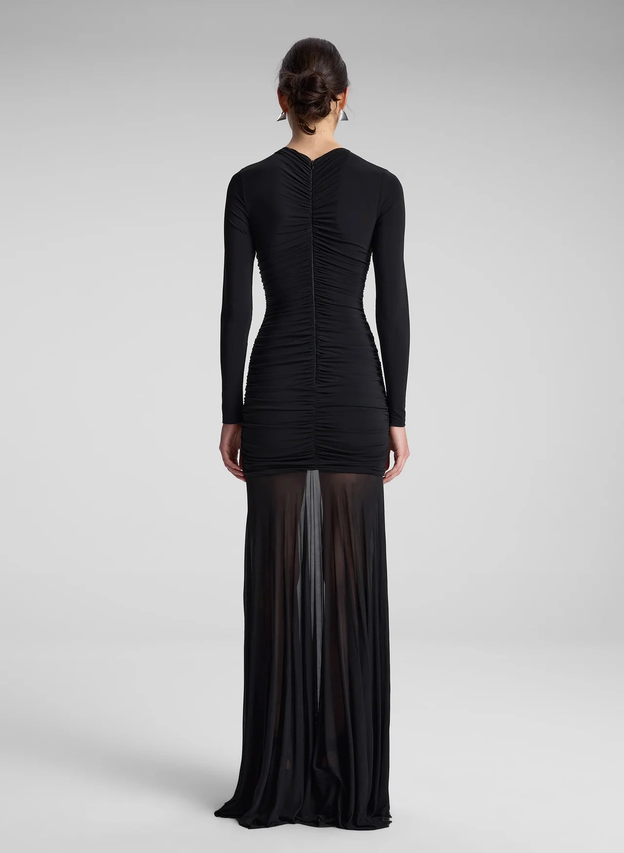 The Fawn Ruched Mesh Maxi Dress combines elegance and contemporary design through its sheer jersey fabric in timeless black. This full-length gown showcases a v-neckline with a delicately ruched bodice that enhances the silhouette, complemented by sheer sleeves for subtle sophistication. The pleated sheer skirt moves gracefully, offering fluidity and refined style suitable for formal occasions or evening wear.