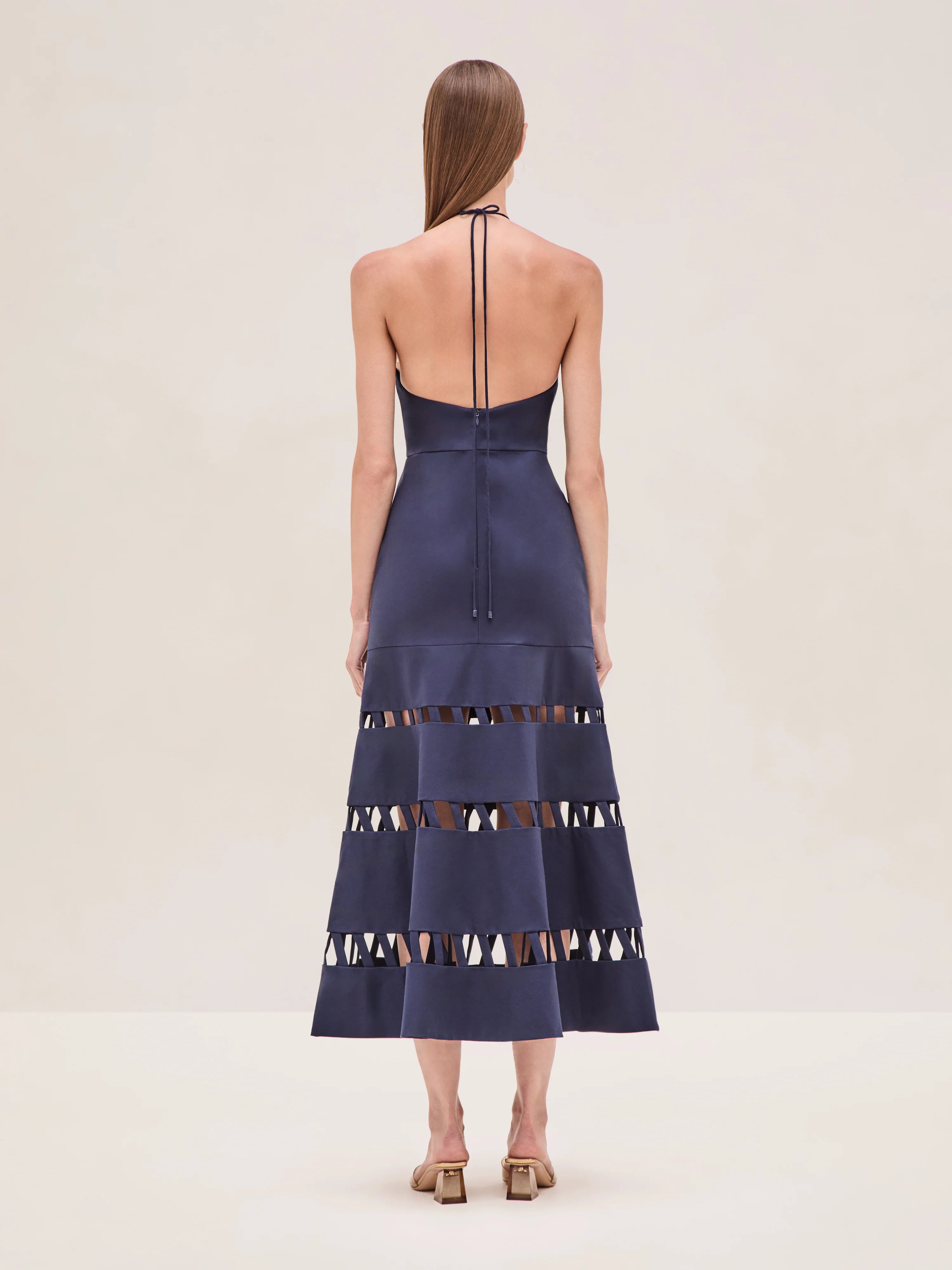 The Janessa Dress by Alexis combines classic comfort with modern detail through its breathable cotton fabric and halter neckline. Its midi length offers versatile styling options, while the distinctive cut-out ladder detailing adds an elegant touch of texture and visual interest, making it a refined choice for warm-weather occasions.