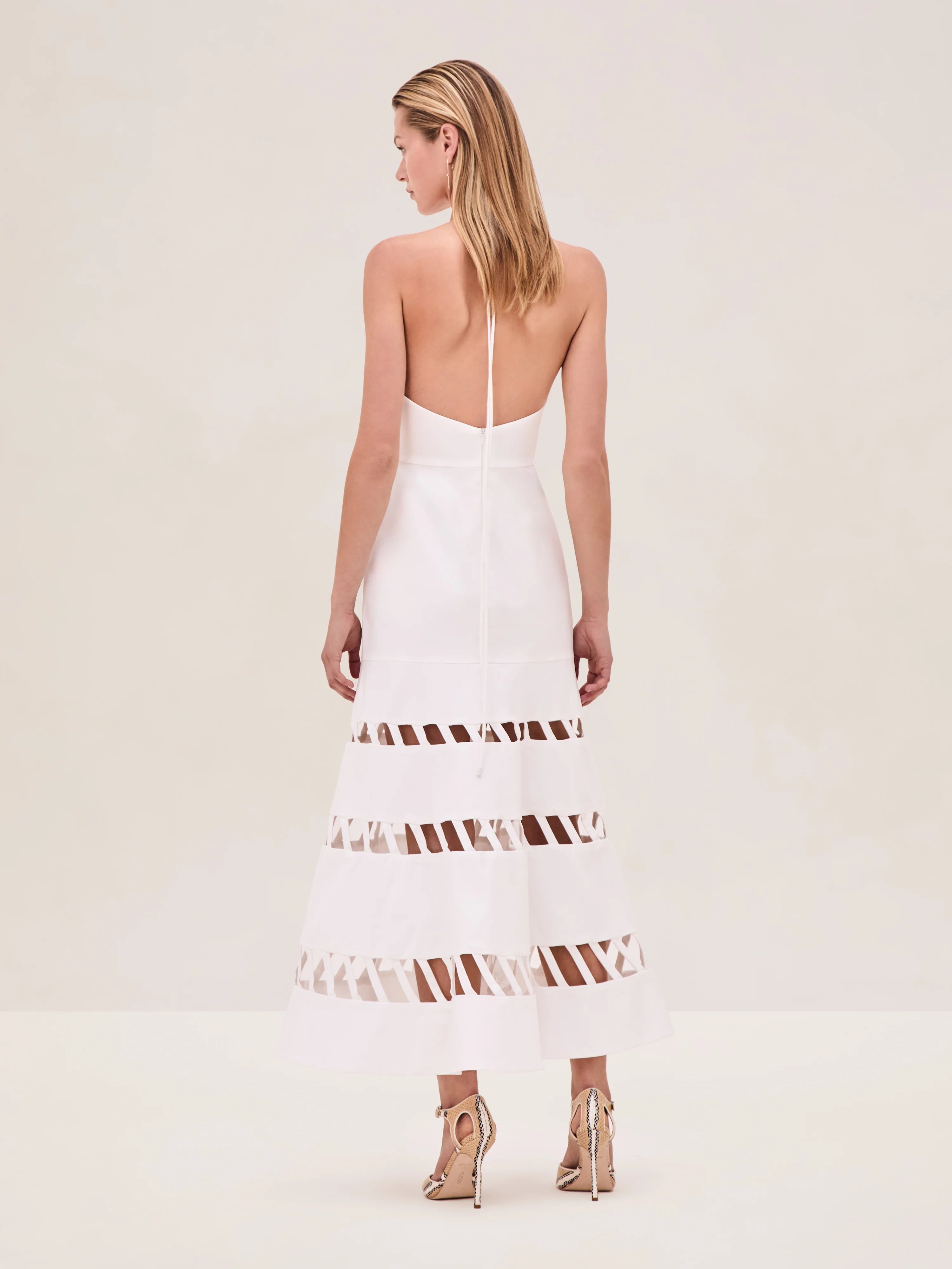The Janessa Dress by Alexis combines classic comfort with modern detail through its breathable cotton fabric and halter neckline. Its midi length offers versatile styling options, while the distinctive cut-out ladder detailing adds an elegant touch of texture and visual interest, making it a refined choice for warm-weather occasions.