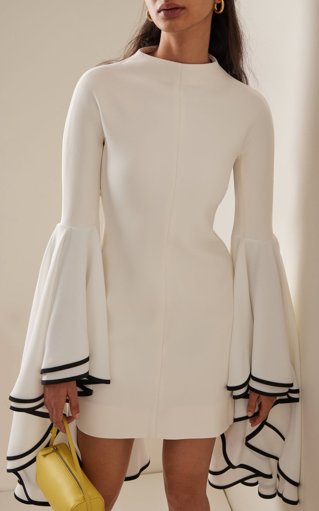 This Stretch Crepe Sleeve Dress by Proenza Schouler features a slim fit with a mock neck and exaggerated bell sleeves accented by contrast cuff trim. The mini hem and concealed back zip create a streamlined silhouette, designed to fit true to size. Pair it with statement heels in a matching colorway and style your hair in a sleek low bun for an elegant, polished look. Unlined for lightweight comfort, it’s perfect for occasions that call for refined sophistication.