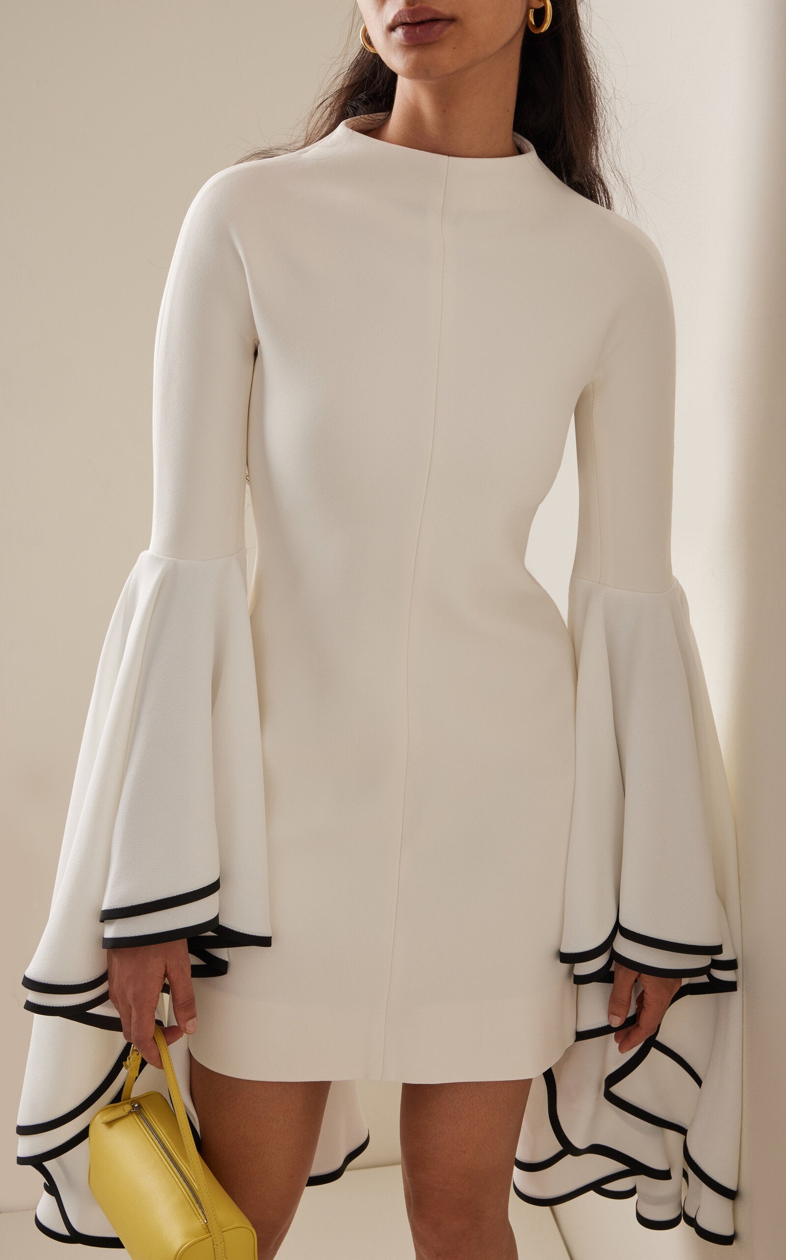 This Stretch Crepe Sleeve Dress by Proenza Schouler features a slim fit with a mock neck and exaggerated bell sleeves accented by contrast cuff trim. The mini hem and concealed back zip create a streamlined silhouette, designed to fit true to size. Pair it with statement heels in a matching colorway and style your hair in a sleek low bun for an elegant, polished look. Unlined for lightweight comfort, it’s perfect for occasions that call for refined sophistication.