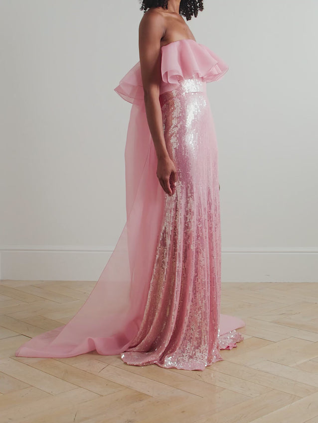 Discover enchantment in Jenny Packham's Galactic gown, where thousands of sequins shimmer and dance with every movement. Crafted from luxuriously fluid satin, this strapless masterpiece features a delicate chiffon trim at the neckline that adds ethereal grace. The floor-sweeping hem creates an elegant silhouette perfect for unforgettable evenings. The stunning Blossom pink shade pairs beautifully with gold jewelry for a radiant, sophisticated look.
