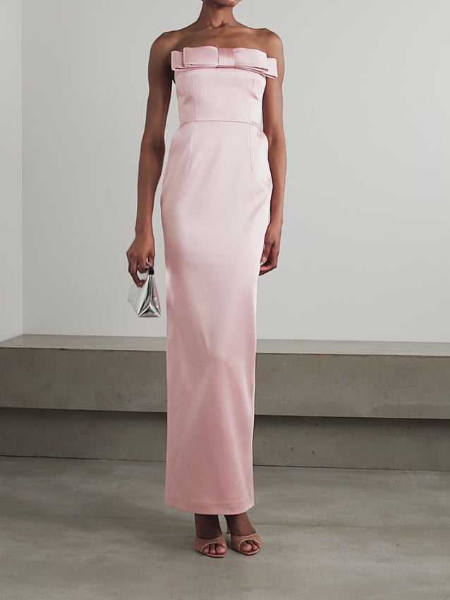 The 'Sisu' gown embodies refined sophistication with its smooth satin construction and strapless, form-fitting bodice. A striking oversized bow detail adorns the bodice, flowing into a streamlined column skirt that creates an elegant silhouette. The delicate 'Boise de Rose' shade pairs beautifully with tonal lip and blush for a cohesive, polished look. Perfect for special occasions where understated luxury meets modern design.