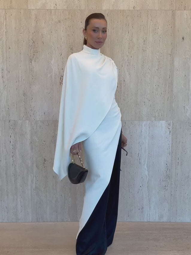 The Wilhelmina Cape Top combines effortless elegance with modern design. This unlined piece features a dramatic draping cross-shoulder shawl silhouette that creates fluid movement with every step. The ruched bodice adds dimension and flattering texture, while the asymmetric hem delivers an unexpected edge. A convenient back zipper closure ensures easy wear. Perfect for layering or wearing solo, this versatile top transitions seamlessly from day to evening.