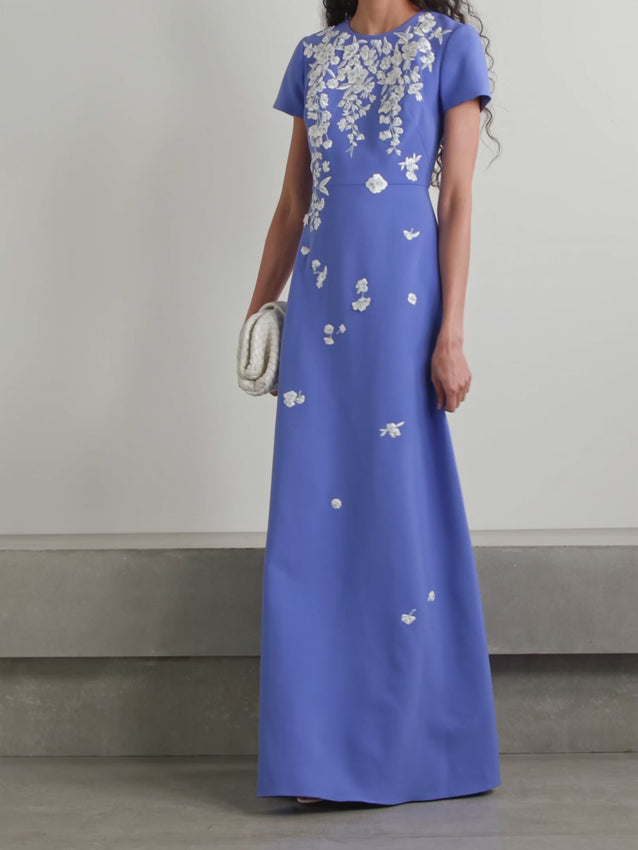 Escape to the French Riviera with this enchanting crepe gown from Carolina Herrera. Crafted from smooth stretch-crepe, the silhouette showcases cascading bouquets of embroidered blooms across the bodice and skirt. A delicate teardrop cutout at the back and a charming trio of bows create an unforgettable finish. Perfect for garden parties, destination weddings, or any occasion calling for effortless elegance and romantic flair.