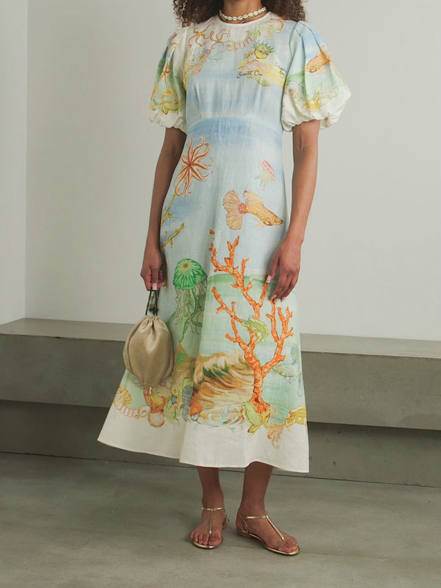 Effortless elegance meets artistic vision in this printed linen-gauze midi dress. Featuring a picturesque seascape by artist Sam Pauletto, the Emerald Cove design captures coastal beauty in rich, captivating detail. Gathered puffed sleeves add romantic dimension, while the airy fabric ensures breathable comfort from morning to evening. Transition seamlessly from day to night—pair with beaded sandals and a raffia clutch for an understated, polished look that requires minimal styling effort.