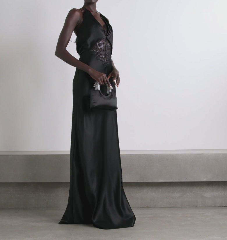 Discover the poetic elegance of the Maria gown, inspired by Emily Dickinson's treasured collection of pressed flowers. This sophisticated black silk-charmeuse gown features delicate metallic lace trims that echo botanical beauty with understated grace. The dramatic plunging halter neckline commands attention, while the gracefully sculpted low back reveals an unexpected allure.