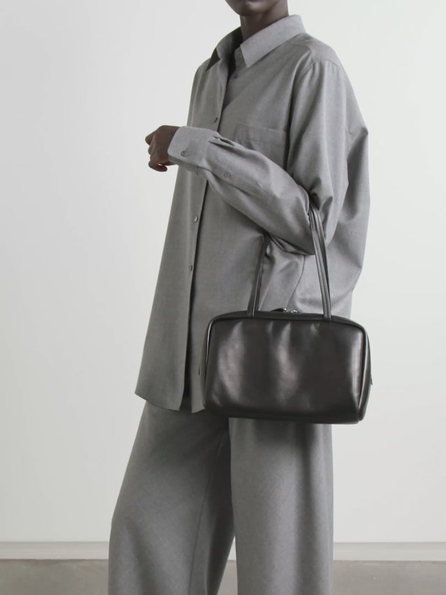 Soft bowling bag in textured calfskin leather with turned-edge construction, elongated flat handles, and dual zipper closure. Minimally finished, the natural grain surface is left intact, giving the leather a supple hand and refined texture that develops character over time.