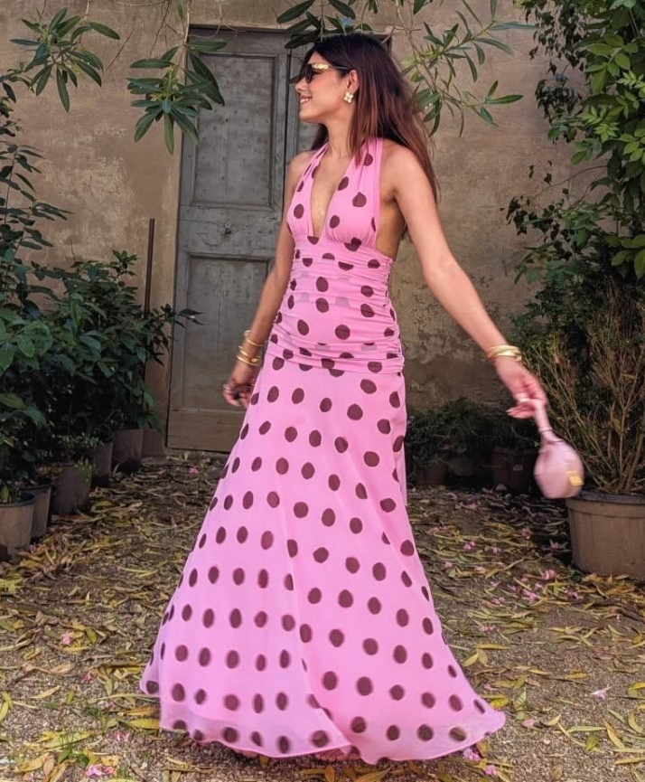 This elegant pink polka dot maxi dress features a chic halter neck design with a flattering V-neckline and a sleeveless, backless silhouette perfect for summer evenings. The pleated skirt adds sophisticated movement while the lace-up detail enhances the fit for added comfort. Ideal for holiday or evening occasions, this dress combines classic patterns with modern design for a refined and stylish look.