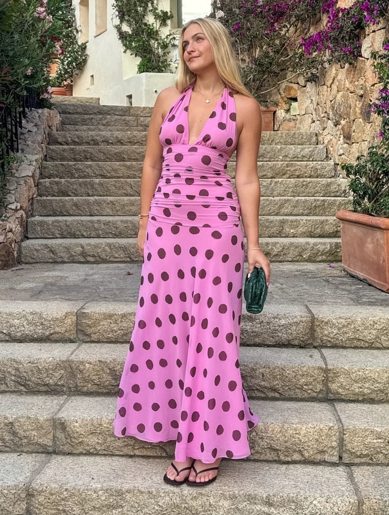 This elegant pink polka dot maxi dress features a chic halter neck design with a flattering V-neckline and a sleeveless, backless silhouette perfect for summer evenings. The pleated skirt adds sophisticated movement while the lace-up detail enhances the fit for added comfort. Ideal for holiday or evening occasions, this dress combines classic patterns with modern design for a refined and stylish look.