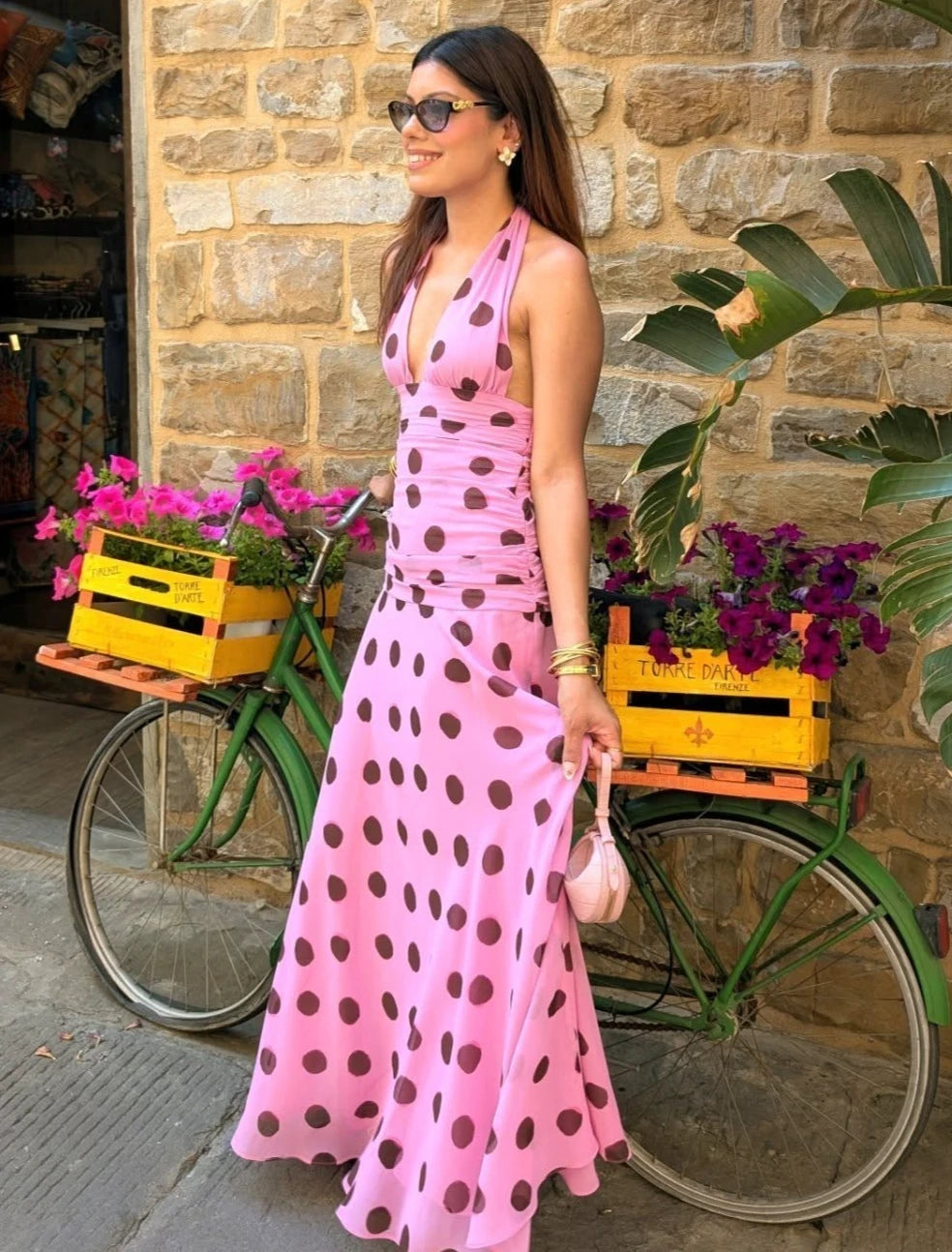 This elegant pink polka dot maxi dress features a chic halter neck design with a flattering V-neckline and a sleeveless, backless silhouette perfect for summer evenings. The pleated skirt adds sophisticated movement while the lace-up detail enhances the fit for added comfort. Ideal for holiday or evening occasions, this dress combines classic patterns with modern design for a refined and stylish look.